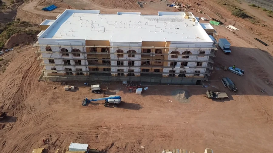 Aerial construction photograph showing a long apartment building, scaffolding and its light-colored roof.