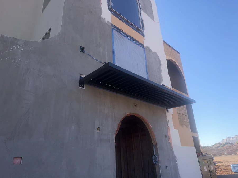 Construction photograph looking up at the installed black metal entry canopy above an unfinished arched doorway.
