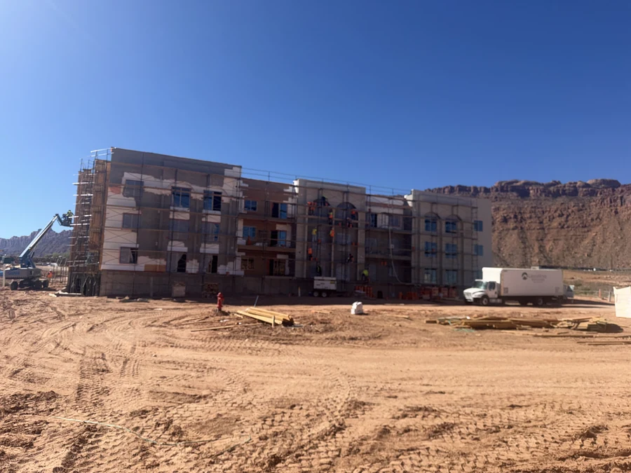 Wide construction photograph of the long apartment façade and graded ground in front of it.